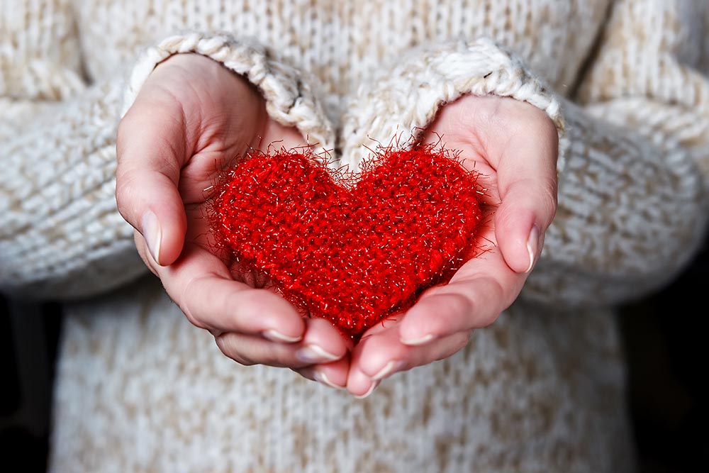 Junge Frau hält zum Valentinstag ein rotes Herz aus Garn in ihren Händen der Kamera entgegen