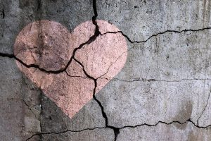 ein gebrochenes rosa Herz auf grauem Beton der von Rissen durchzogen ist und das Liebeskummer und Trennung repräsentiert