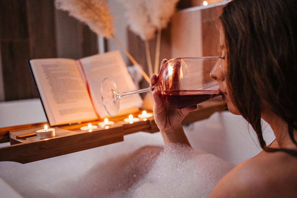 Junge Frau feiert den Valentinstags mit Selbstliebe mit einem Glas Wein und einem entspannenden Schaumbad