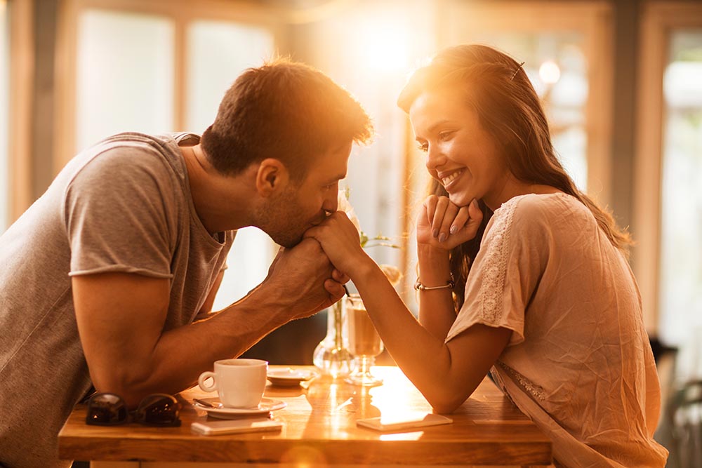 Junges Paar flirtet im Restaurant und Mann küsst Hand der lächelnden Frau