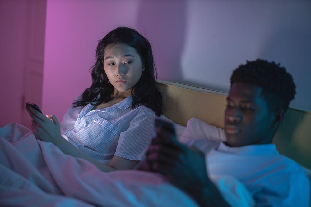 Junge asiatische Frau liegt neben ihrem jungen schwarzen Mann im Bett und blickt eifersüchtig zu ihm