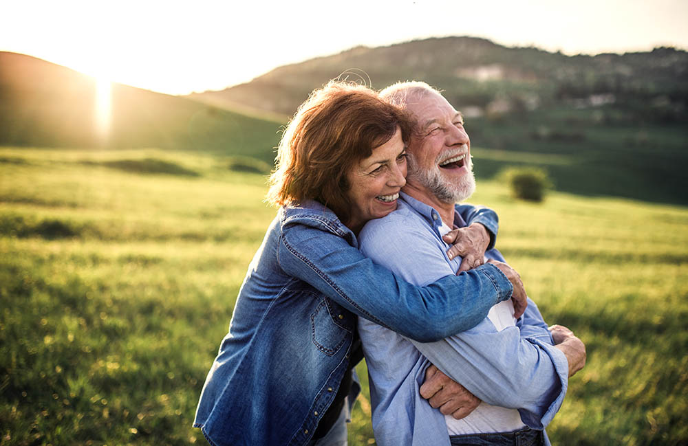 Frau und Mann im mittleren Alter umarmen sich glücklich lachend auf einer grünen Wiese