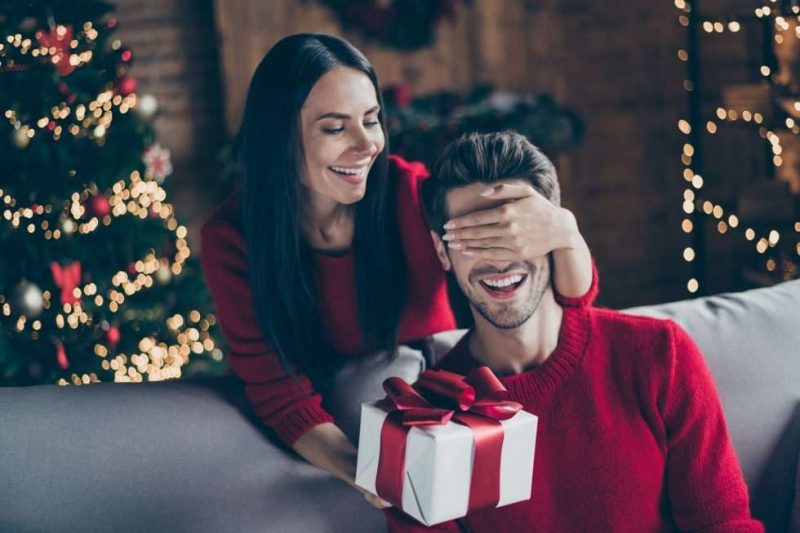 Junge Frau gibt ihrem Partner Weihnachtsgeschenke für Männer