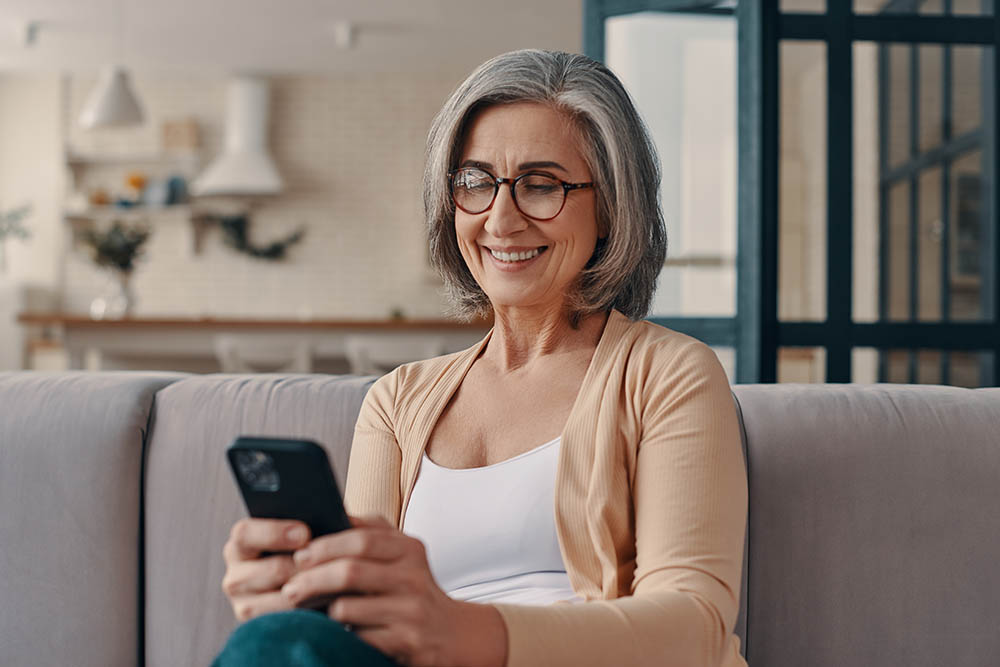 Ältere Frau sieht nach Ende der Kontaktsperre glücklich lächelnd auf ihr Handy