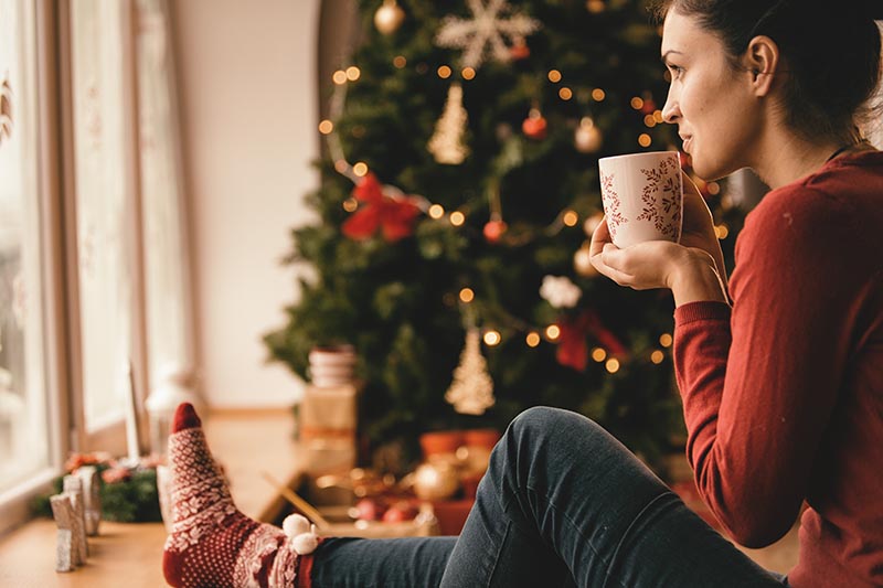 Junge Frau feiert Weihnachten alleine und verwöhnt sich mit einer Tasse Tee