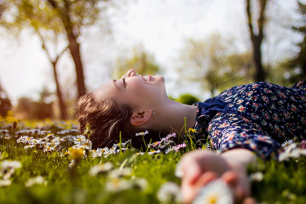 Frau liegt lachend im Sonnenschein im Gras und hat alles zum glücklich werden