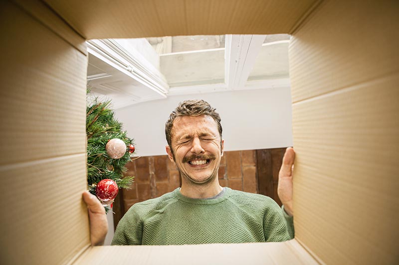 Mann öffnet ein No-Go Weihnachtsgeschenk für Männer und schneidet eine lustige Grimasse