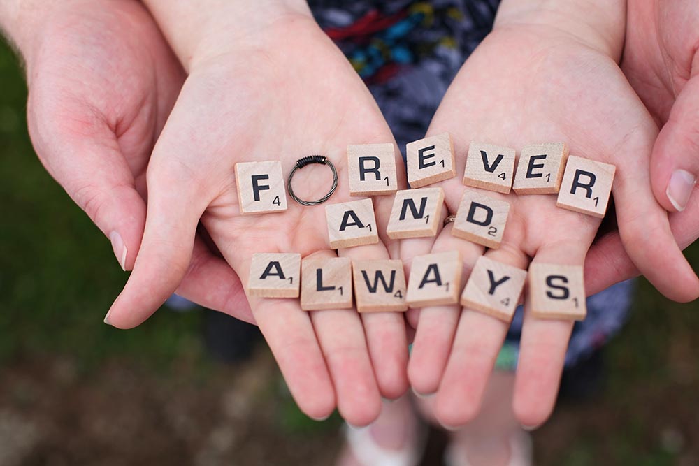 Hände eines Mannes und einer Frau mit Scrabble-Steinen die Liebe für immer und ewig buchstabieren