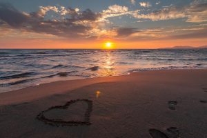 Romantischer Sonnenuntergang am Meer und Strand mit Herz im Sand zum Valentinstag