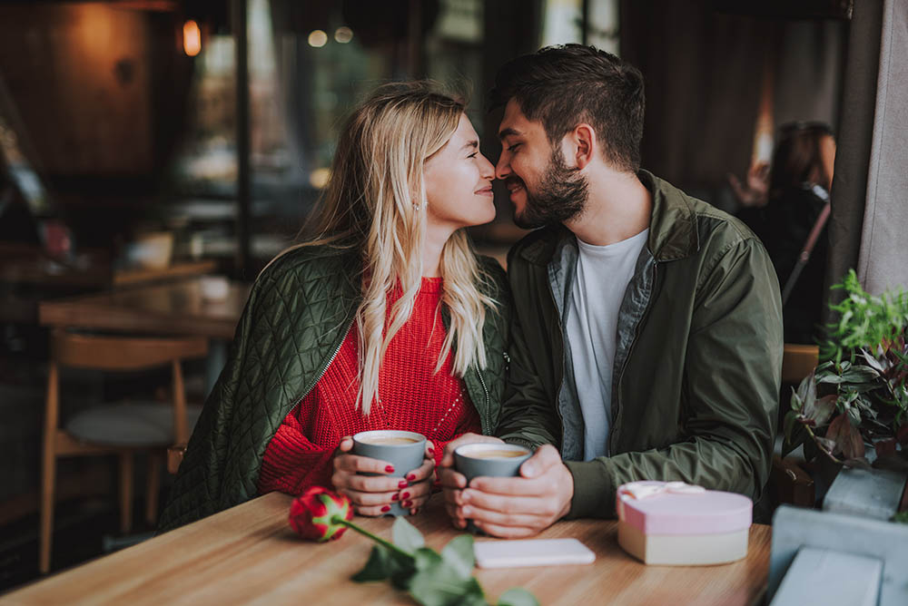 junges Paar sitzt verliebt lächelnd Nase an Nase in einem Cafe weil sie sich als Seelenpartner erkennen