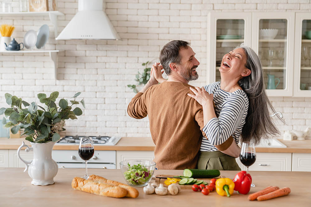glücklich verliebtes Paar im mittleren Alter tanzt als Dualseelen lächelnd durch die Küche