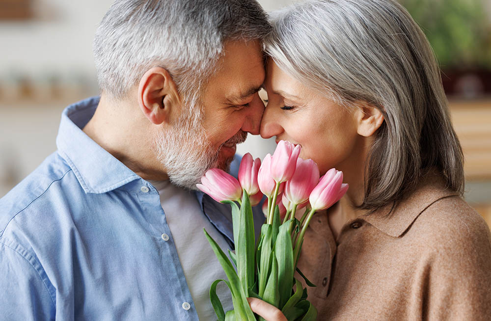 älteres Paar Mann und Frau in Seelenpartnerschaft lehnt verliebt Stirn an Stirn und hält einen Strauß Blumen
