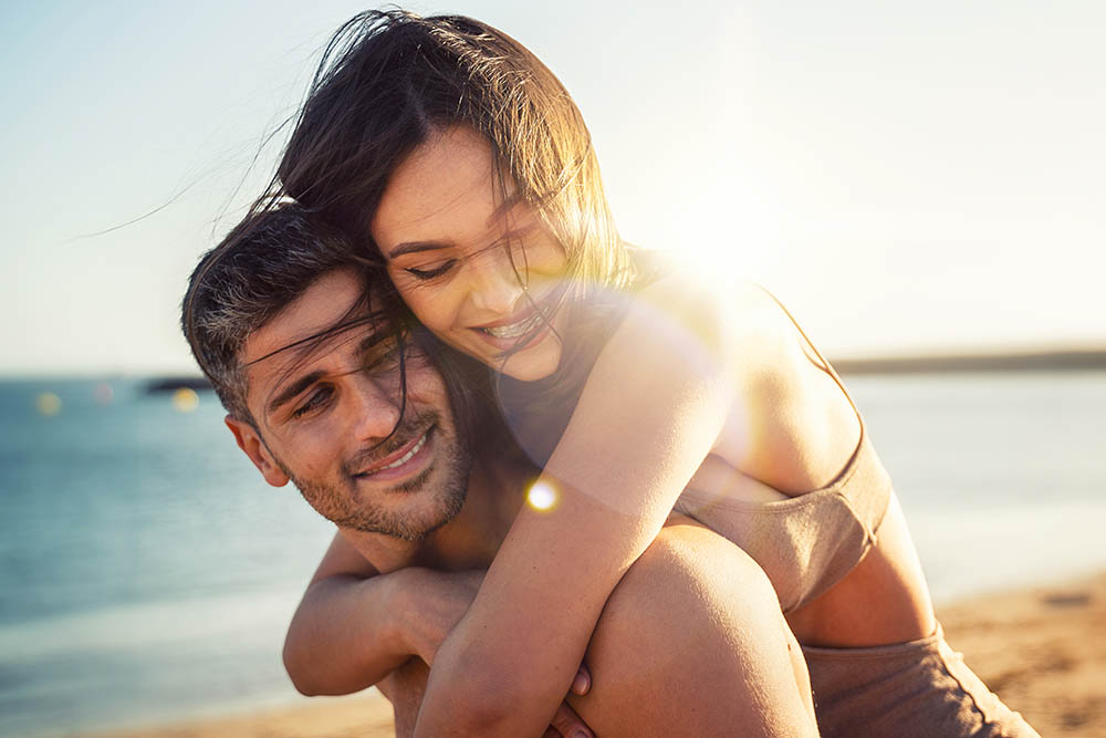 Junger Mann und junge Frau umarmen sich in Liebe an einem sonnigen Strand