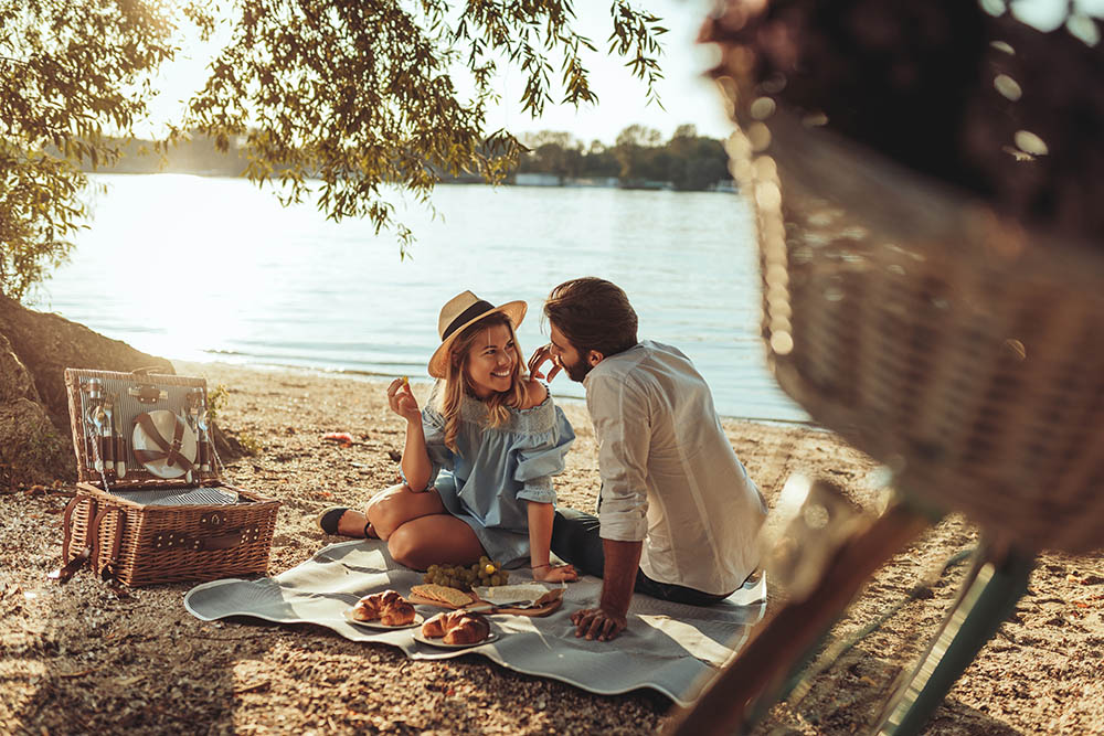 junge Frau und junger Mann essen verliebt ein Picknick am Strand