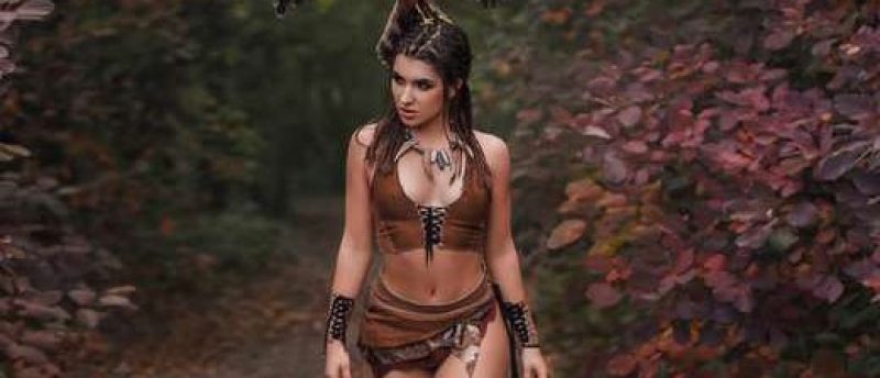 Aggressive-sexual wild girl, wanders in the jungle with a tamed bird. Princess warrior in a brown leather suit, with a short skirt, top and wrist cups. Background autumn landscape. Hairstyle dreadlocks. Artistic Photography